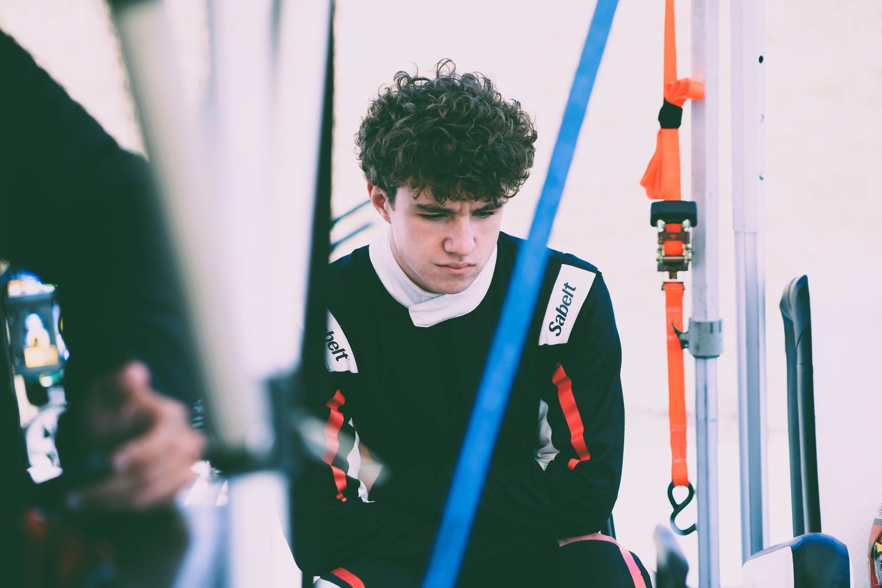 A young driver looks down in the pit lane, gathering himself before a session.