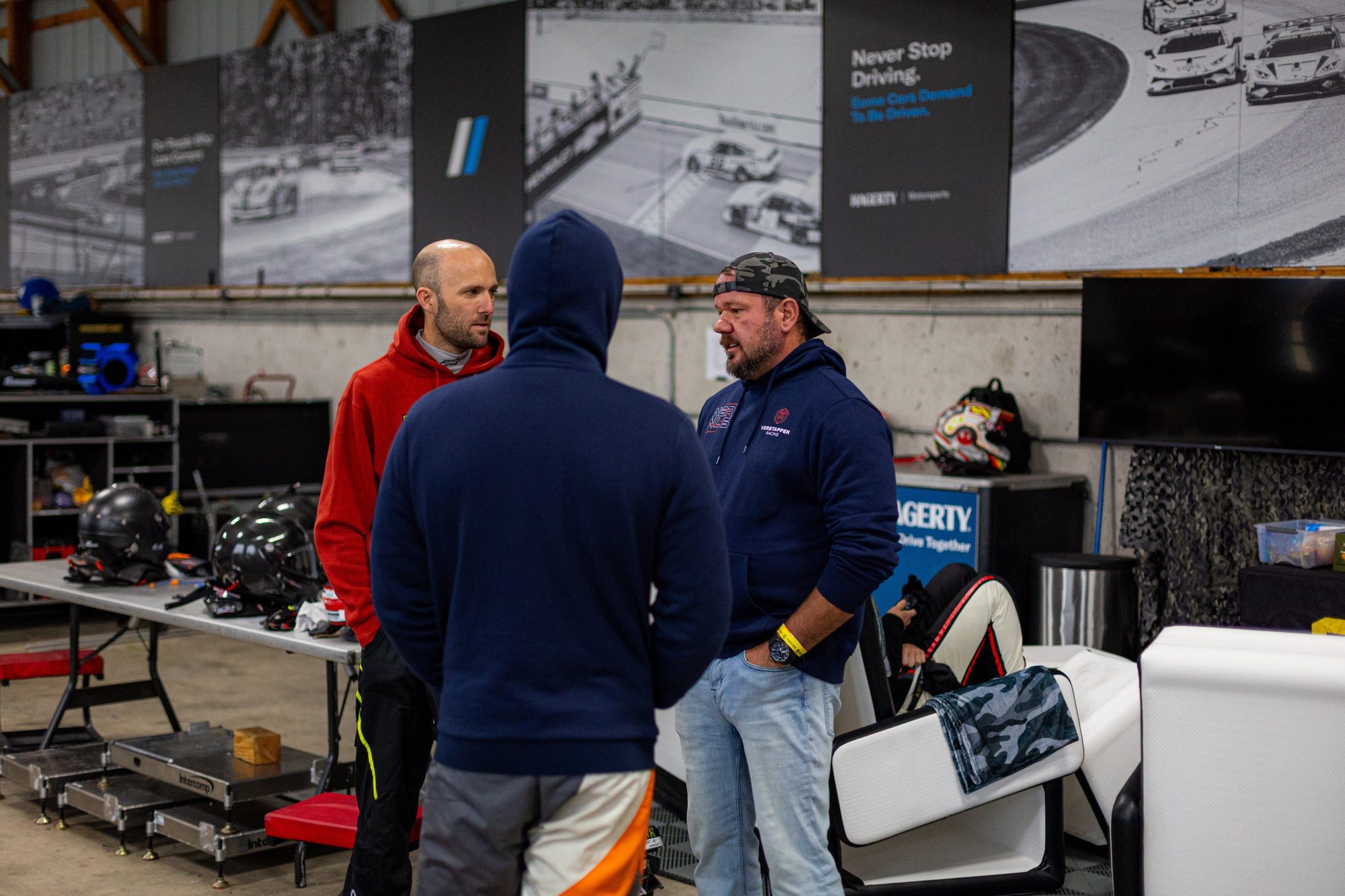 Three men talk in the garage, helmets on the table beside them.