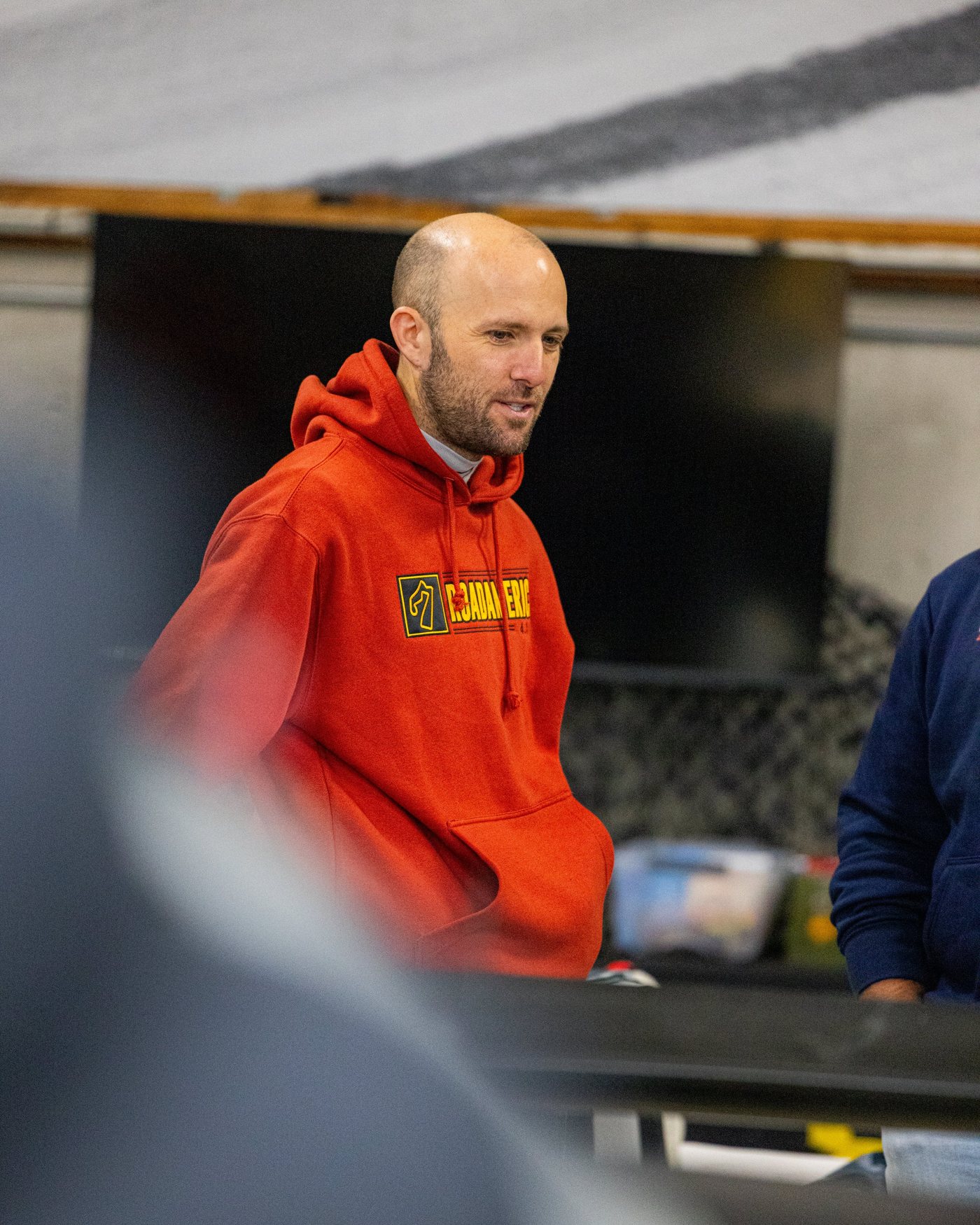 A man in a red hoodie stands in the garage, looking off to the side.