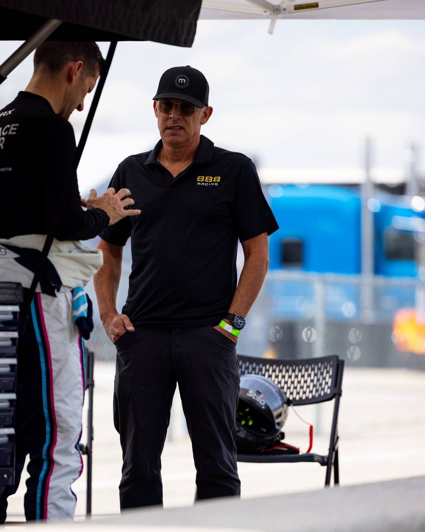 A man in an 888 Racing shirt stands under the awning, talking with a driver.