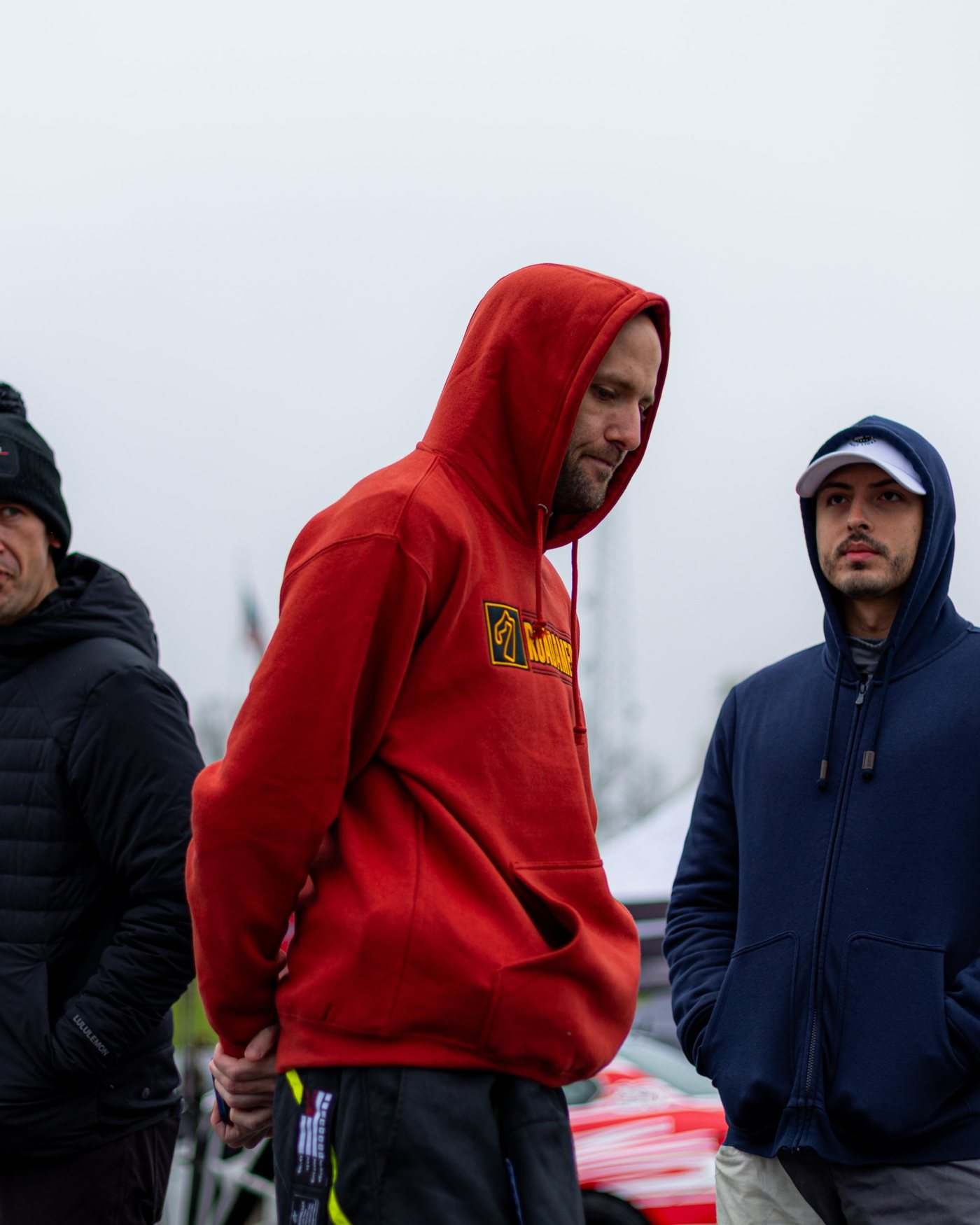 Three people stand in the paddock with their hands in their pockets, tents behind them.